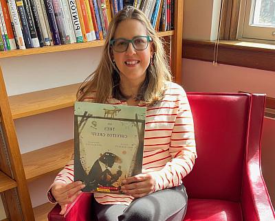 Woman sits in a red upholstered chair holding a copy of 三只公山羊